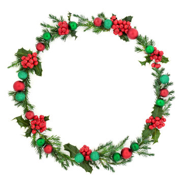 Christmas wreath abstract decoration with winter flora of juniper fir and holly with red and green baubles on white background with copy space. Decorative symbol for the festive season.