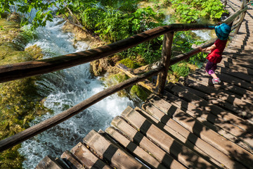 Little girl looking through the balustrade and watching the rushing water splashing down the mossy rocks at the Plitvice Lakes National Park, Croatia