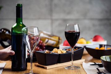 Red wine pouring into a wine glass at a tasting with various types of appetizers. 