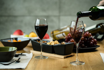 Red wine pouring into a wine glass at a tasting with various types of appetizers. 