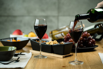 Red wine pouring into a wine glass at a tasting with various types of appetizers.  - 293964097