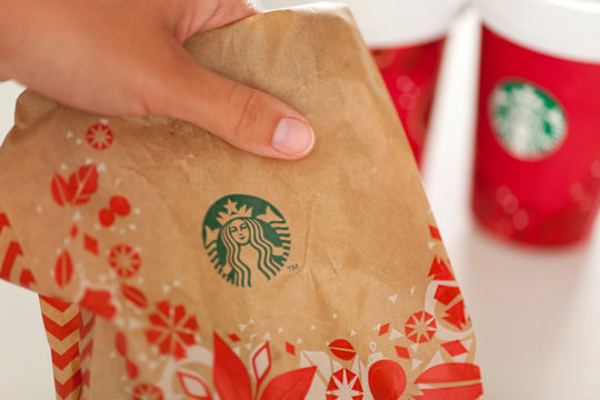 Paphos, Cyprus - November, 14 2013 Christmas holiday takeaway from Starbucks. Woman hand takes Starbucks holiday paper pack with muffin. Two paper cups of espresso on background.