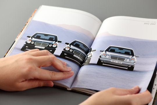 Tambov, Russian Federation - November 3, 2012 Woman browses a catalog at a Mercedes-Benz cars dealership. She opens pages with three cars, which produced in 1995-2002. Studio shot. 