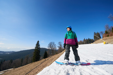 Young sportive athletic female snowboarder in helmet standing on snowy track on copy space...
