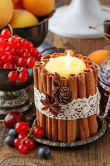 Candle decorated with cinnamon sticks among autumn fruits and flowers.