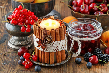 Candle decorated with cinnamon sticks among autumn fruits and flowers.