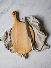 Wooden cutting board on kitchen napkin and metal knife on a gray background