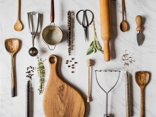 Flat lay various metal, wooden kitchen tools and dry spices in glass tube and raw herbs on a marble...