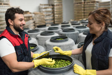 Worker woman looking into a barrel and talking with male partner in olives storage company