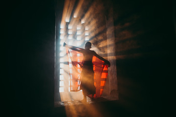 Children monk praying at the buddhist temple. artistic portrait with a monk silhouette in the mist and light filtering from a window