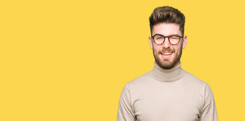 Young handsome business man wearing glasses winking looking at the camera with sexy expression,...