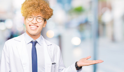 Young handsome scientist man wearing glasses smiling cheerful presenting and pointing with palm of hand looking at the camera.