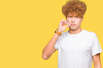 Young handsome man with afro hair wearing casual white t-shirt mouth and lips shut as zip with...