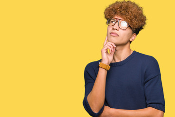 Fototapeta na wymiar Young handsome man with afro wearing glasses with hand on chin thinking about question, pensive expression. Smiling with thoughtful face. Doubt concept.