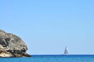 sailboat sailing ship on the sea still water with blue sky and rocks mediteranean sea