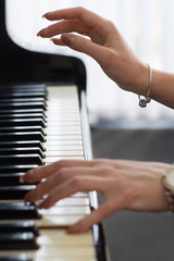 Fototapeta premium Woman playing on grand black piano closeup. Shallow depth of field. Female fingers with a musical instrument.