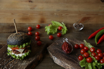 black sandwich, hamburger or burger with beef or chicken, tomatoes, onions, chili, cheese, lettuce and a sesame bun on a wooden rustic board. Fast food concept. With copy space for text