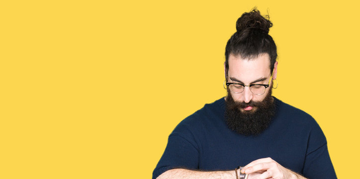 Young hipster man with long hair and beard wearing glasses Checking the time on wrist watch, relaxed and confident