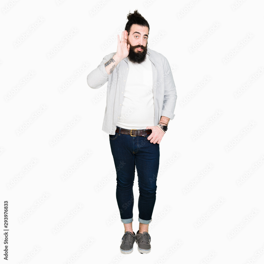 Wall mural young man with long hair, beard and earrings smiling with hand over ear listening an hearing to rumo