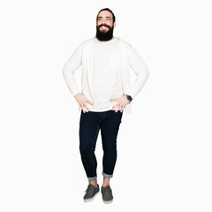 Naklejka premium Young man with long hair and beard wearing sporty sweatshirt looking away to side with smile on face, natural expression. Laughing confident.
