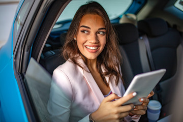 Smiling casual girl sitting in back seat using tablet PC