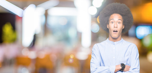 Young african american man with afro hair afraid and shocked with surprise expression, fear and excited face.