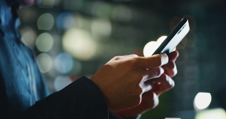 Slow motion close up of an young man hands using a smartphone phone in a center of the city by night. - Powered by Adobe