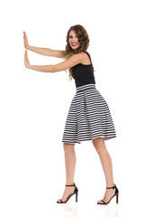 Smiling Young Woman In Dress And High Heels Is Pushing Something