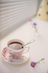 Black tea in an elegant vintage porcelain cup and spoon on the white windowsill