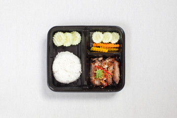Fried Pork with Garlic and Pepper and rice put in black plastic box, put on a white tablecloth, food box, Thai food.