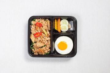 Rice mixed with basil and snakeskin gourami with fried egg put in black plastic box, put on a white tablecloth, food box, Thai food.