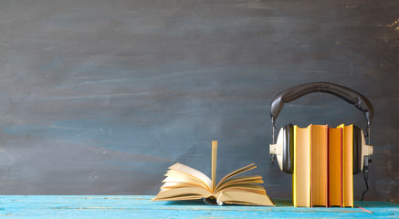 audio book concept with open book, row of books and headphones, panorama format on grungy...