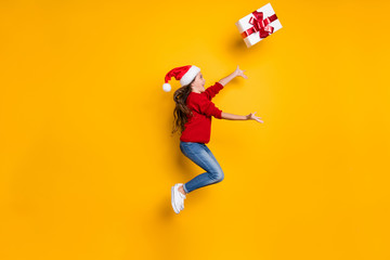Fototapeta na wymiar This box is mine. Full body profile photo of crazy little lady jumping high catching big giftbox wear red knitted pullover and jeans isolated yellow background