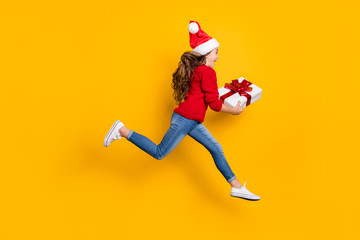 Fototapeta na wymiar Full size profile photo of crazy little lady jumping high taking giftbox from santa in x-mas midnight wear red knitted pullover and jeans isolated yellow background