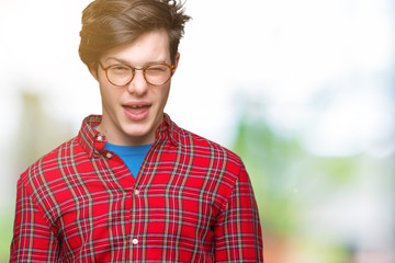 Young handsome man wearing glasses over isolated background winking looking at the camera with sexy...