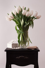 Spring flowers. Bouquet of white tulips in a vase on the bedside table. Shallow depth of field