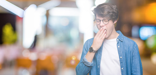 Young handsome man wearing glasses over isolated background bored yawning tired covering mouth with...