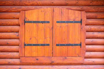 Obraz na płótnie Canvas Wooden window shutters with large iron hinges. Background of red-brown logs and boards. Beautiful pattern and wooden structure.