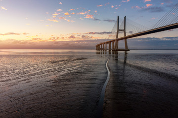 Fototapeta na wymiar Vasco da Gama bridge at sunrise in Lisbon, Portugal. Vasco da Gama Bridge is a cable-stayed bridge flanked by viaducts and rangeviews that spans the Tagus River in Parque das Nações in Lisbon.