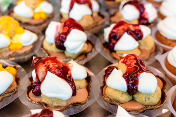 Close up of profiteroles, cream puffs or chou à la crème with whipped cream and strawberry jam, in displayed for sale at an weekend street market, selective focus