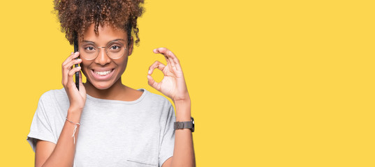 Young african american woman talking on smartphone over isolated background doing ok sign with fingers, excellent symbol