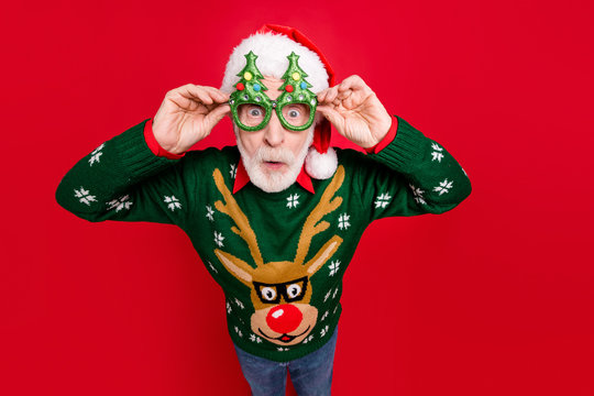 Photo of funny grey haired santa looking on unbelievable low x-mas shopping prices speechless wear x-mas tree shape specs ugly ornament sweater isolated red background