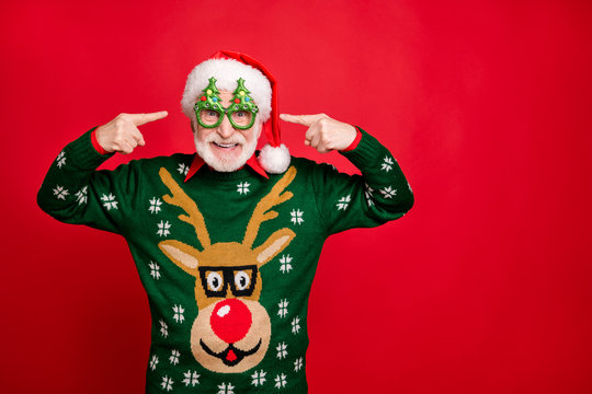 Photo of funny grey haired santa father indicating fingers on cool party specs x-mas tree shape wear ugly ornament reindeer sweater isolated red background