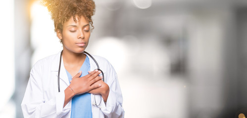 Young african american doctor woman over isolated background smiling with hands on chest with...