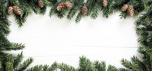 Christmas frame of fir branches and pine cones on white wooden board