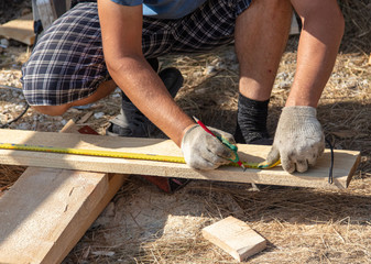 Worker measures a wooden board at a construction site