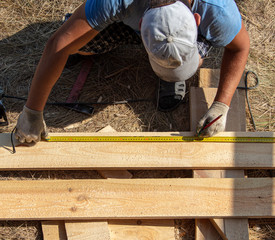 Worker measures a wooden board at a construction site
