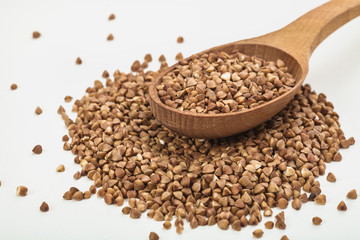 buckwheat in a plate on a white table and in a wooden spoon