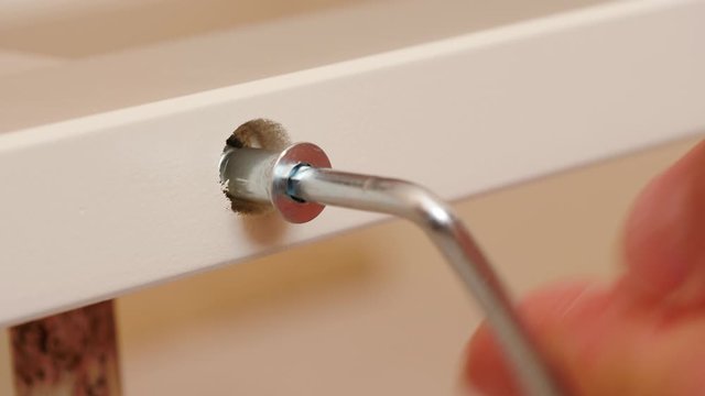 Installation and assembling furniture at home. Male hand with allen key hexagonal tool screwing furniture screw into wooden plank. Do it yourself furniture assembly