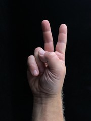 Fototapeta premium Two fingers up, on a black background. A gesture with two fingers, a sign of freedom. Finger sign, male hand pointing up.